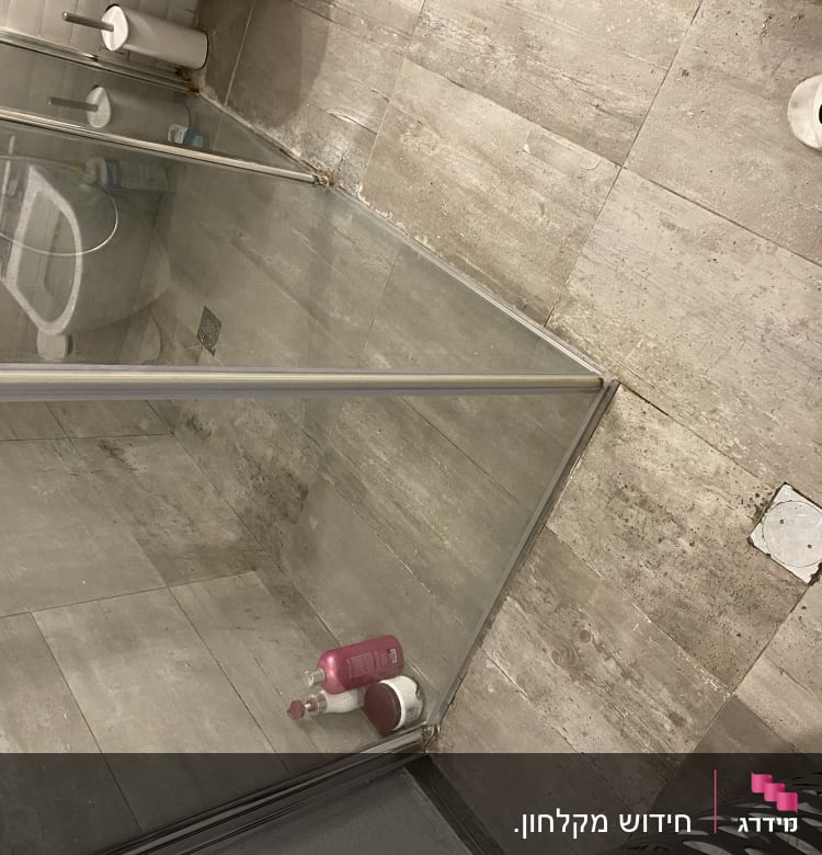 מקלחון זכוכית עם בקבוקי שמפו וסבון על הרצפה